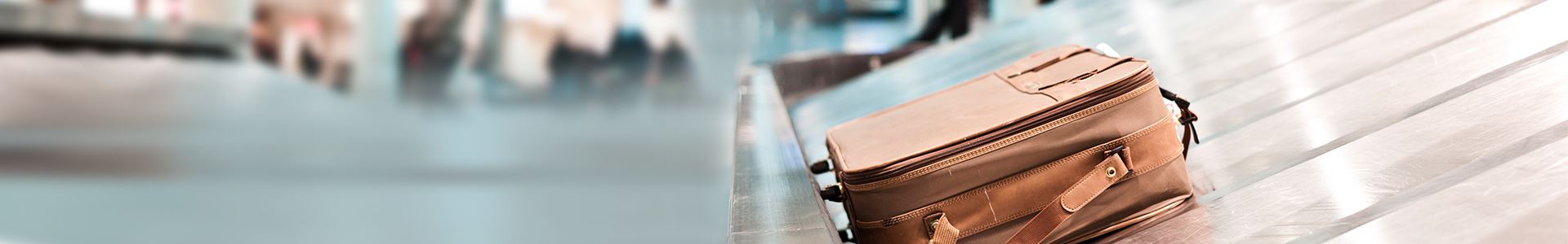 Zdjęcie przedstawia brązową walizkę leżącą na taśmie bagażowej na lotnisku. W pobliżu nie ma innych walizek.