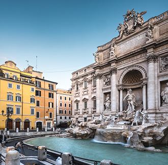 Widok z boku Fontanny di Trevi. Po prawej widać krystalicznie czystą, niebieską fontannę, a tuż za nią Palazzo Poli i jego kamieniarkę. Po lewej stronie znajduje się kilka budynków w odcieniu pomarańczy.