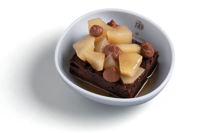 Fotografia de um prato branco com uma pera e um brownie de chocolate e canela. 