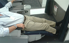 照片中是一名在商务舱就坐的男子，身体呈半躺姿势，双腿舒适伸展，脚上未着鞋袜。 