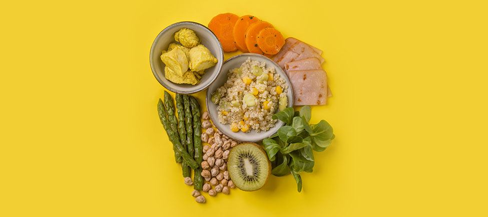 Foto com vários ingredientes que representam uma dieta com pouco sódio contra um fundo amarelo: aspargos, cereais, kiwi, legumes, cenouras e outros ingredientes adequados a esse tipo de dieta.