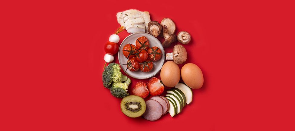Foto com vários ingredientes que representam uma dieta isenta de glúten sobre um fundo vermelho: cogumelos, tomate, brócolos, morangos, kiwi, ovos, pepino e outros ingredientes adequados a este tipo de dieta.