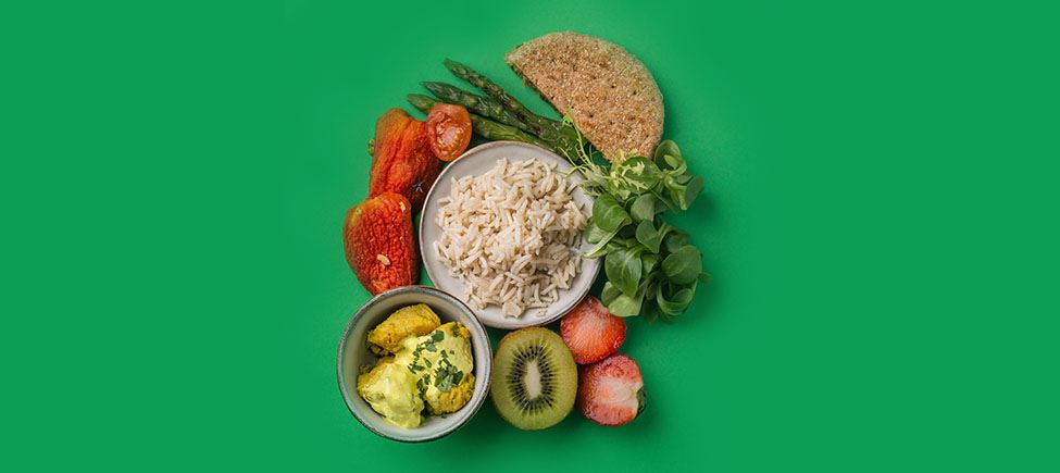 Une photo avec différents ingrédients halal représentant un repas musulman sur fond vert : des tomates, des fraises, des asperges, un kiwi, et d'autres ingrédients adaptés à ce type de régime.