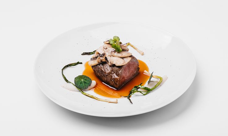 A plate containing milk-fed veal and barbecue with tupinambur puree, garnished with some greens, like leeks. It is a dish signed by Chef Ricardo Costa, from his Taste the Stars repertoire, which serves signature cuisine aboard TAP planes.